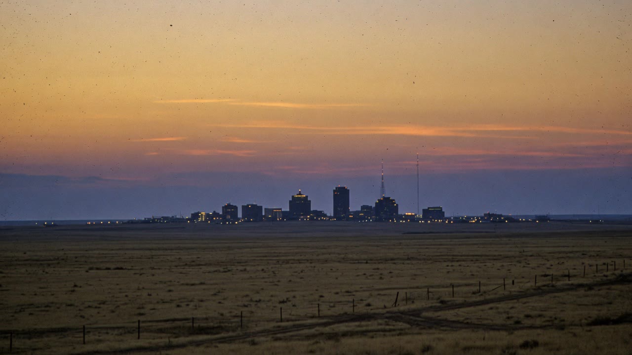 Station artwork: a distant city skyline with radio masts under an amber dusk sky over open plains